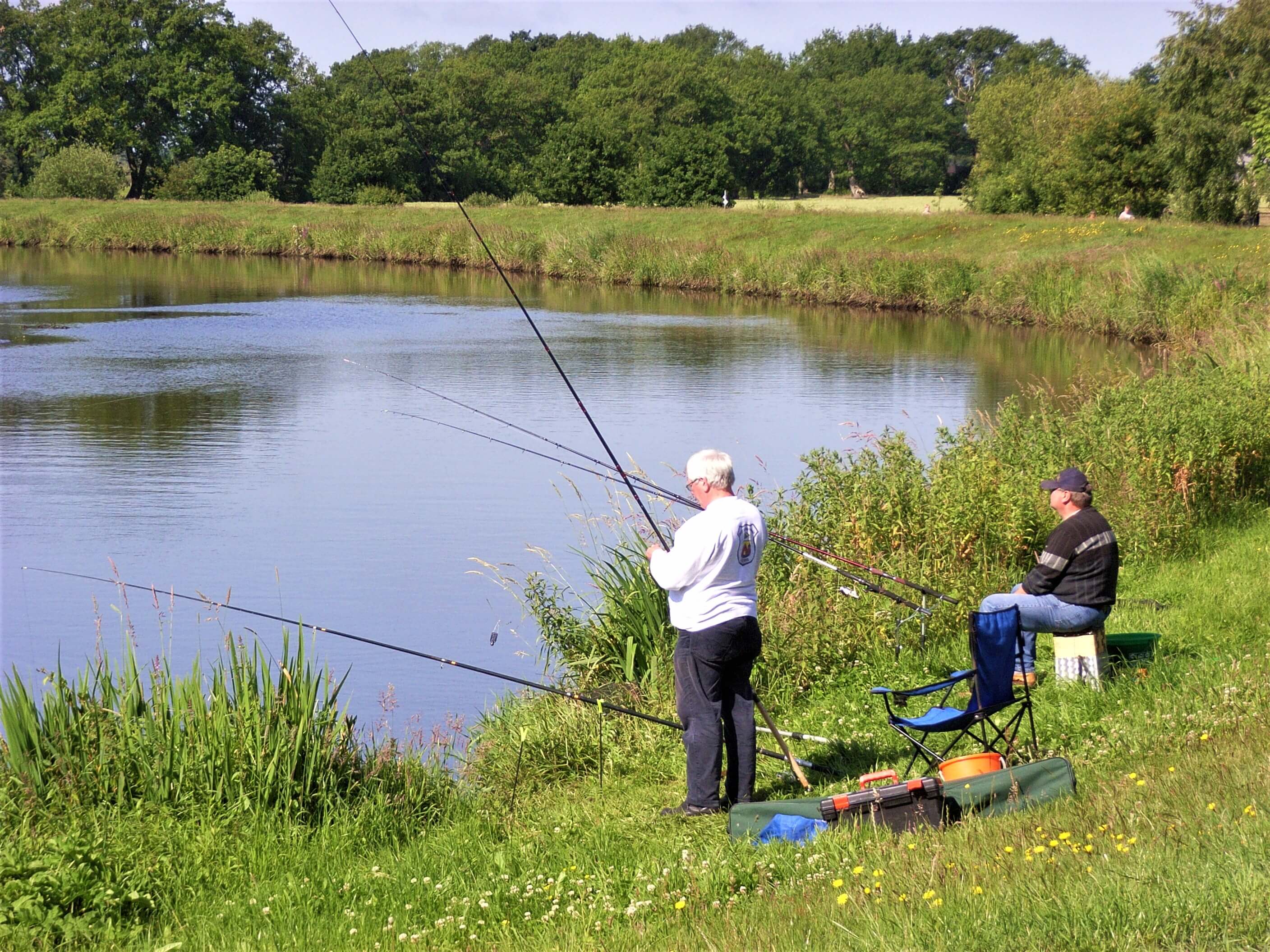 Zwei Angler sitzen am Aper-Tief unter einem grünen Schirm.