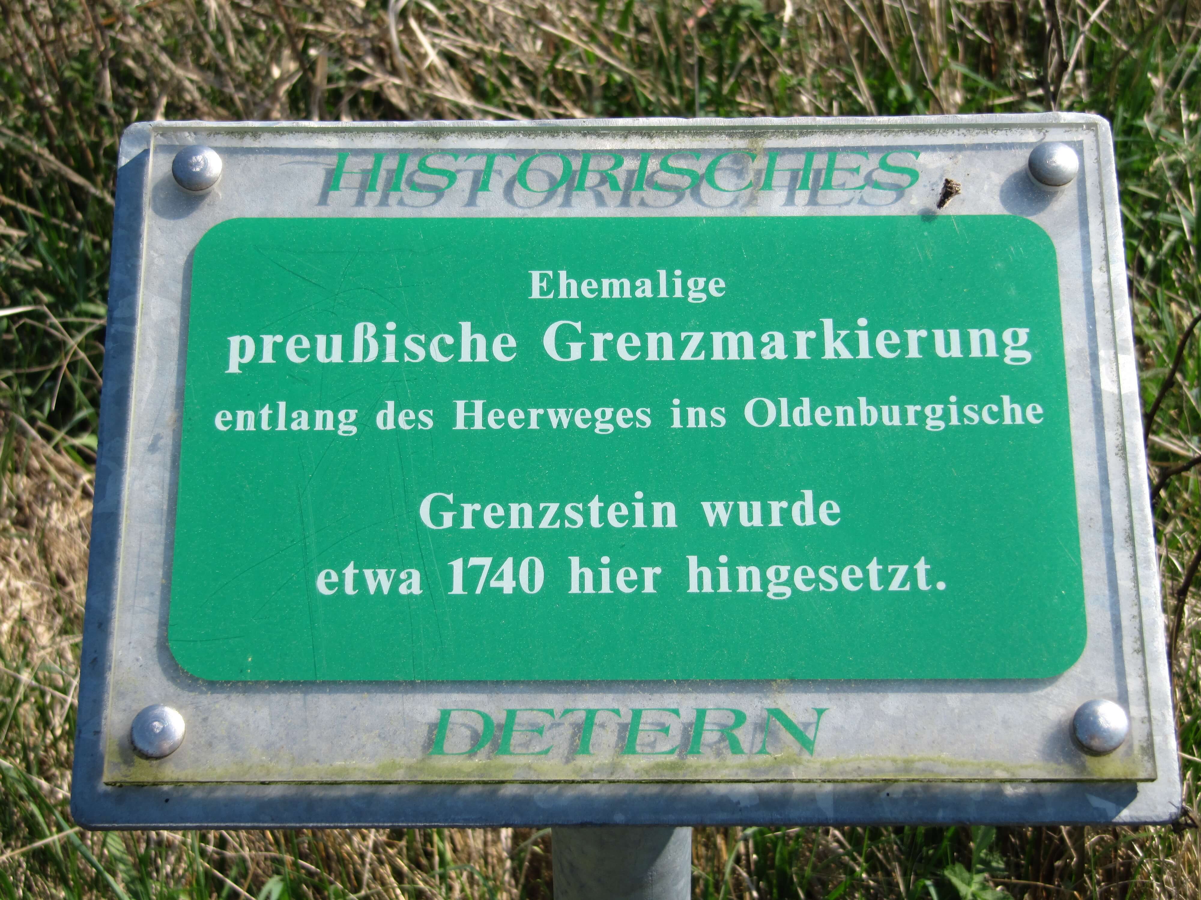 Das Foto zeigt eine grüne Schautafel mit dem Hinweis auf einen ehemaligen Grenzstein