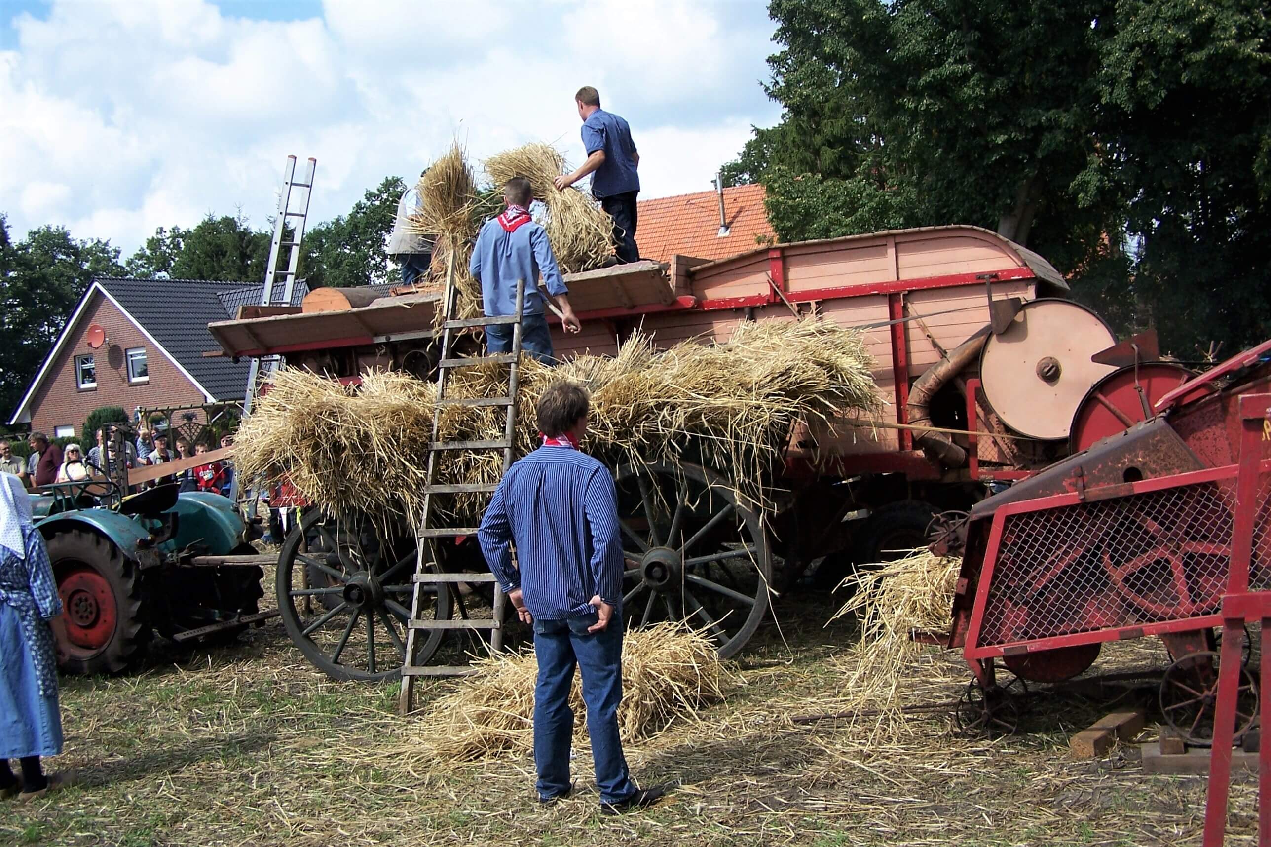 Das Bild zeigt, wie in früheren Zeiten das geschnittene Korn von Bauern auf einen Wagen verladen wurde.