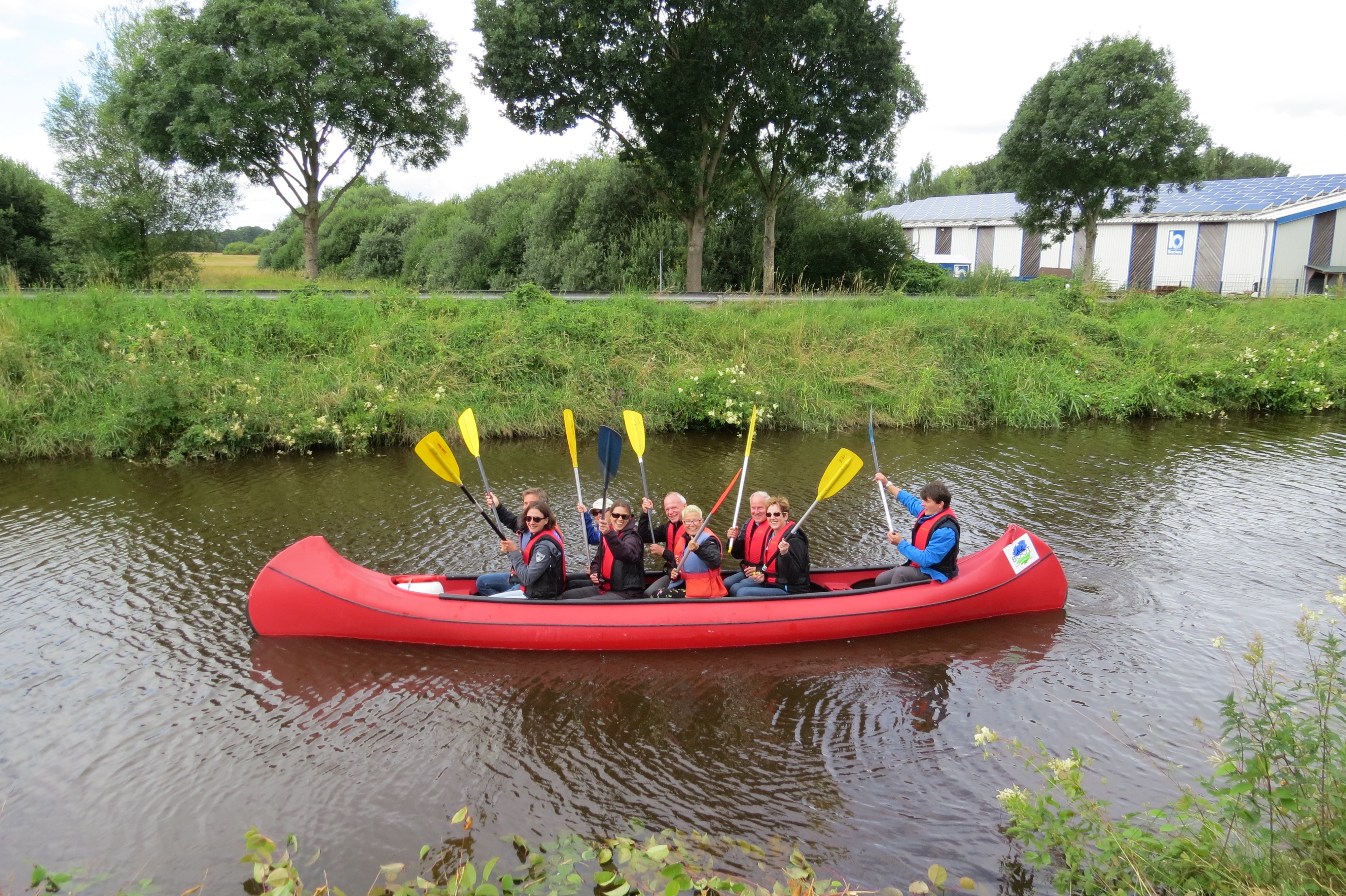 Paddlergruppe im Boot auf dem Augustfehn Kanal heben ihre Paddel zum Gruß