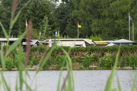 Mobilheime an einem idyllischen Campingplatz, umgeben von grünen Bäumen und Wasser, Fahnen wehen im Wind