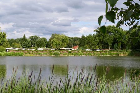 Vor einem sanft wellenden Gewässer liegt ein idyllischer Campingplatz, umrahmt von üppigem Grün.