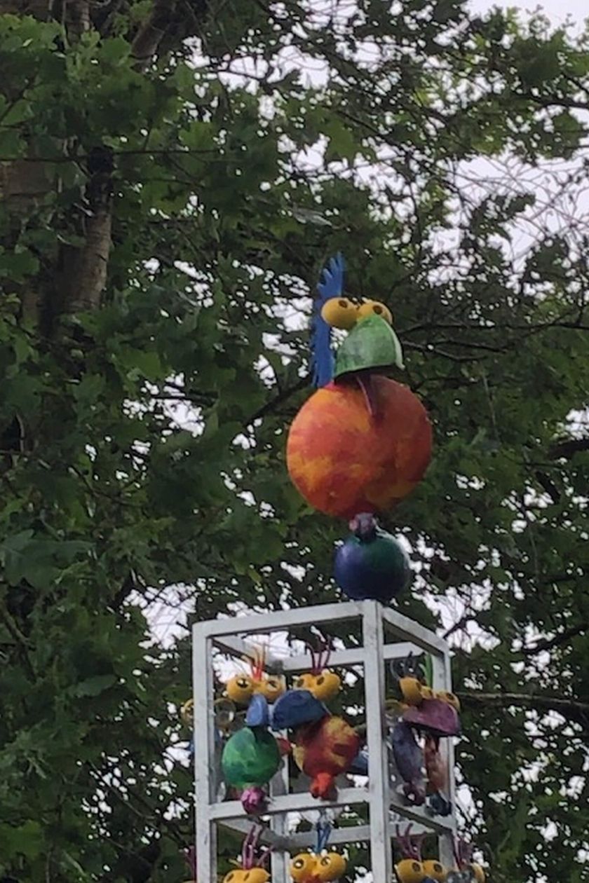 Ein bunter Stahlvogel sitzt auf einer blauen Weltkugel. Im Hintergrund grünes Blattwerk.