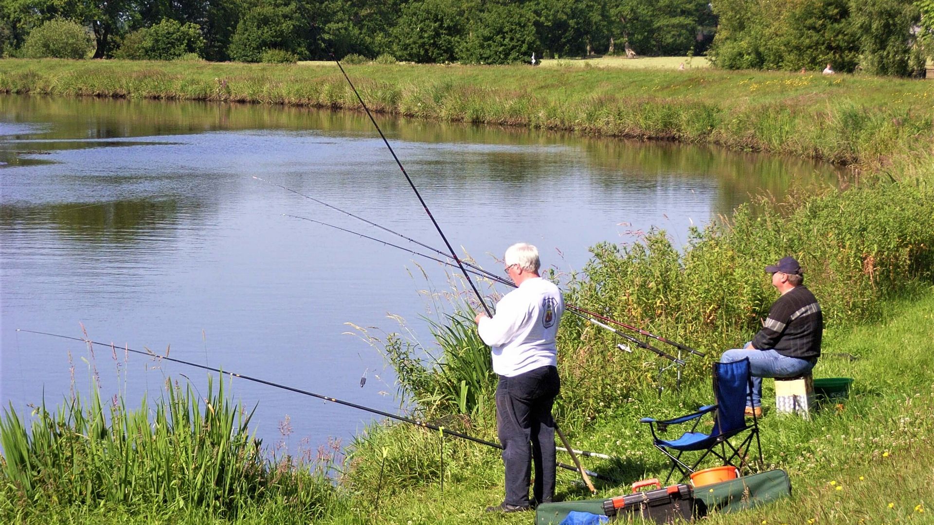 Zwei Angler sitzen am Aper-Tief unter einem grünen Schirm.