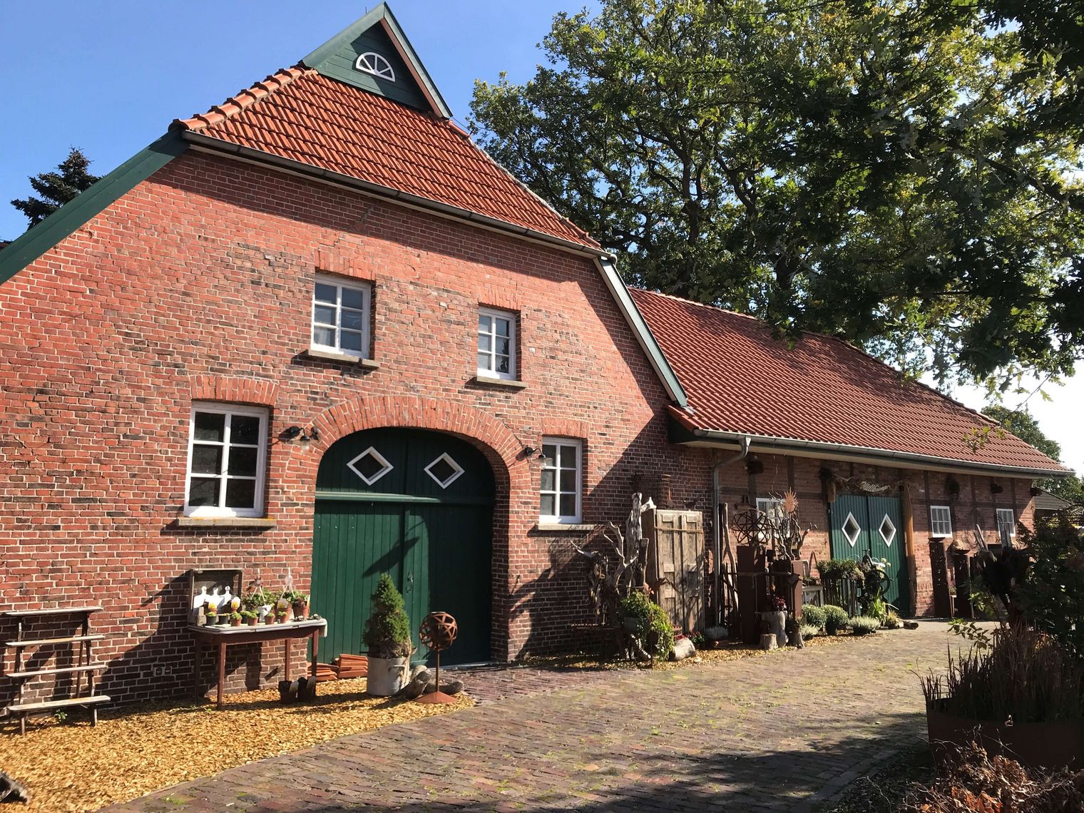 Vor einem alten, hübsch restaurierten Bauernhaus, sind florale Dekorationsartikel und Grünplanzen ausgestellt.
