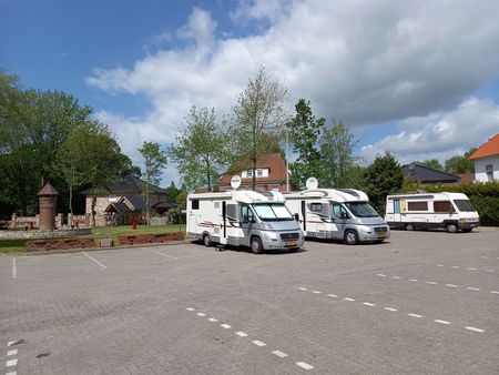 Ein sonniger Stellplatz mit drei Wohnmobilen auf gepflastertem Gelände, umgeben von üppigen grünen Bäumen
