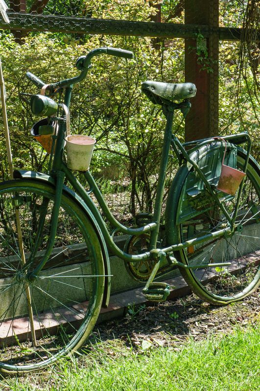 Ein grün angesprühtes Fahrrad lehnt an einem Gitterzaun
