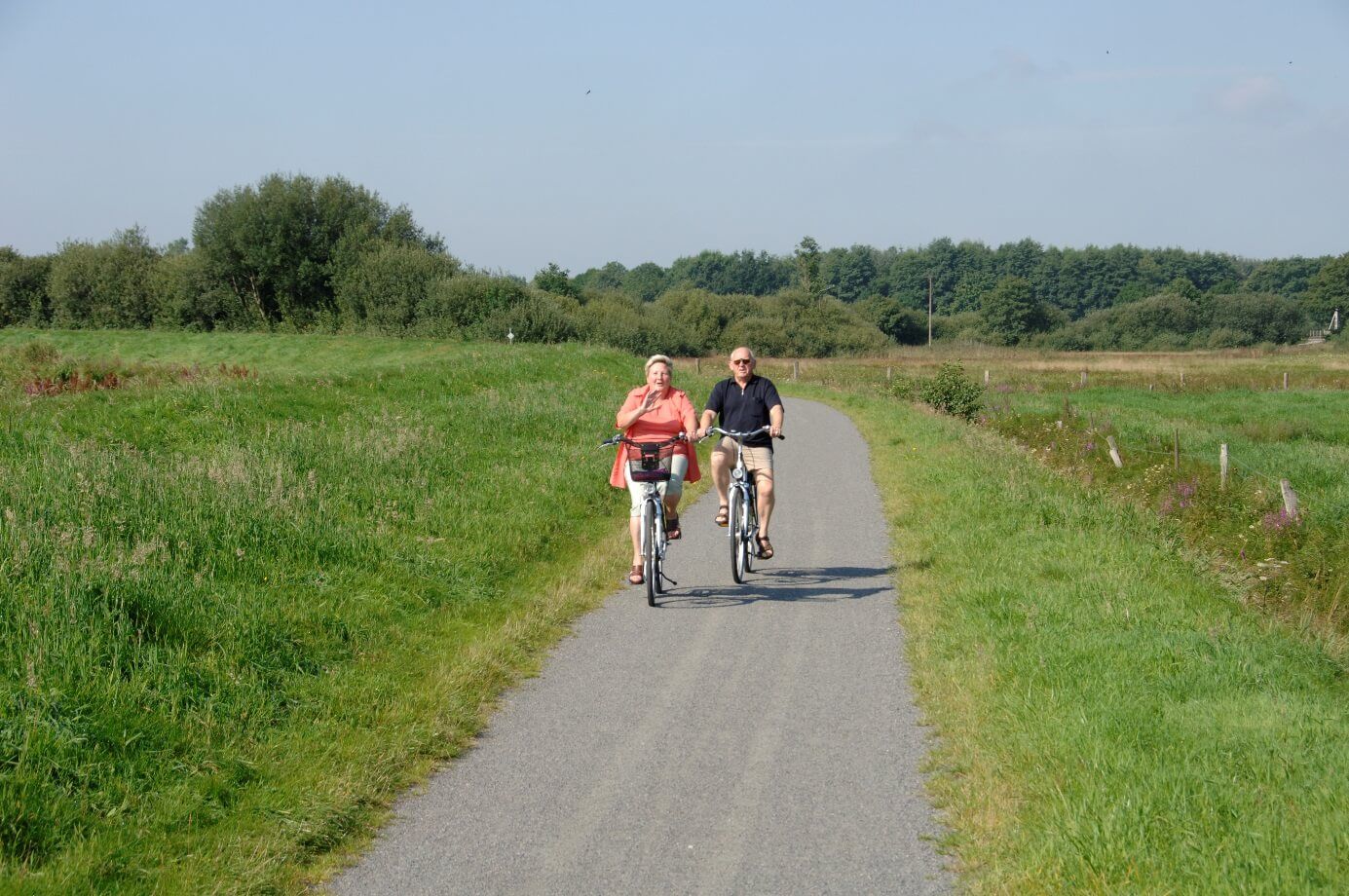 Das Foto zeigt ein Ehepaar von vorne, das auf Fahrrädern entlang des Deiches fährt.