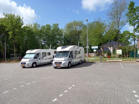 Ein sonniger Stellplatz mit zwei Wohnmobilen auf gepflastertem Gelände, umgeben von üppigen grünen Bäumen
