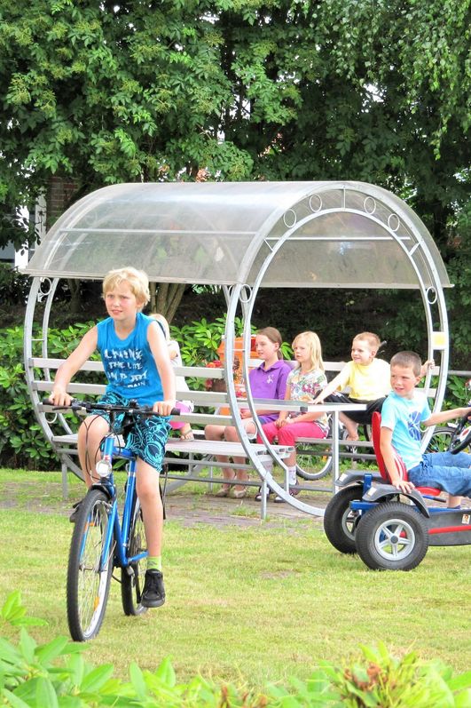 Eine Kindergruppe spielt und rastet auf einer Rasenfläche. Ein Junge fährt Kettcar und ein anderer Fahrrad.