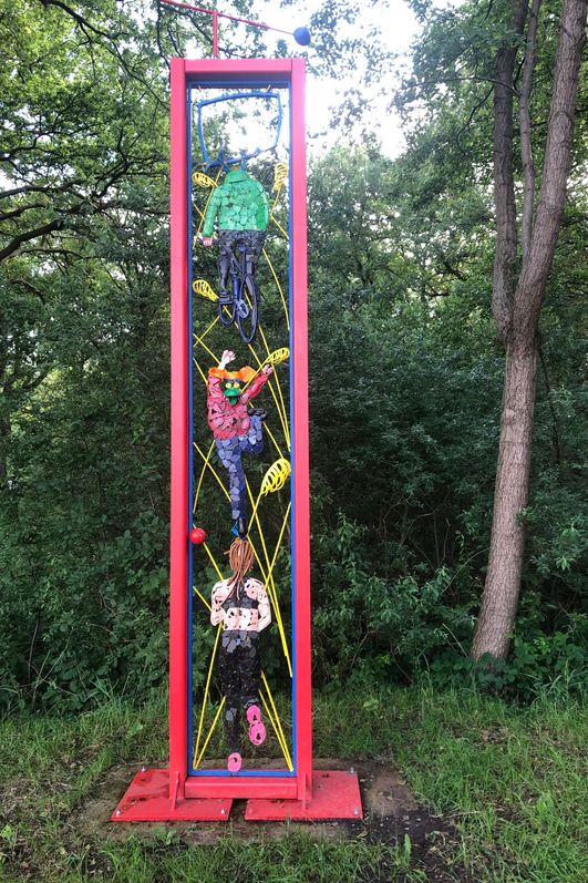 Ein bunter Metalrahmen mit nachgebildeten Tieren als Sportler steht vor einer mit Sträuchern bewachsenen Fläche