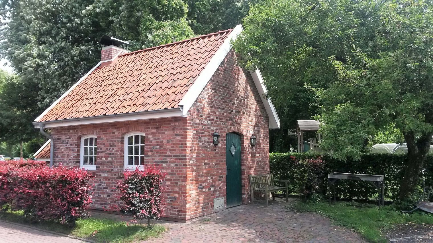 Nachbau eines kleine rot geklinkerten Backhauses nach historischem Vorbild inmitten von belaubten Hecken und Bäumen.