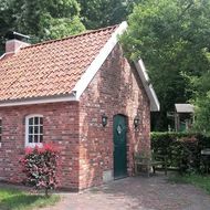 Nachbau eines kleine rot geklinkerten Backhauses nach historischem Vorbild inmitten von belaubten Hecken und Bäumen.