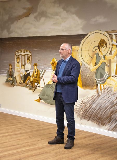 Ein Mann steht vor einem historischen Wandbild mit Strandszene